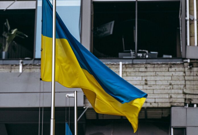 Ukrainas karogs uz sagrautas ēkas fona